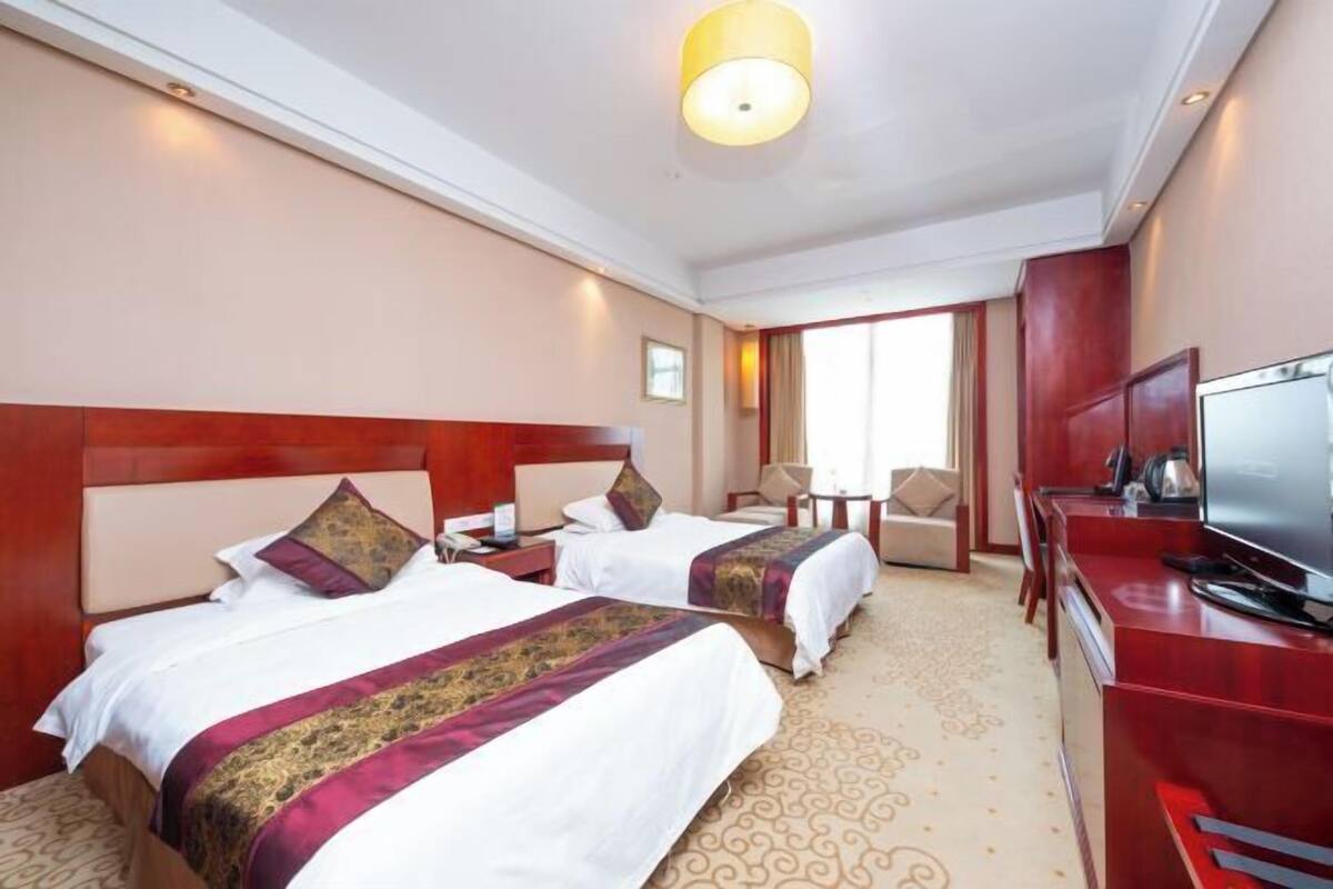 A hotel room with two beds, a TV, a desk, and a chair.