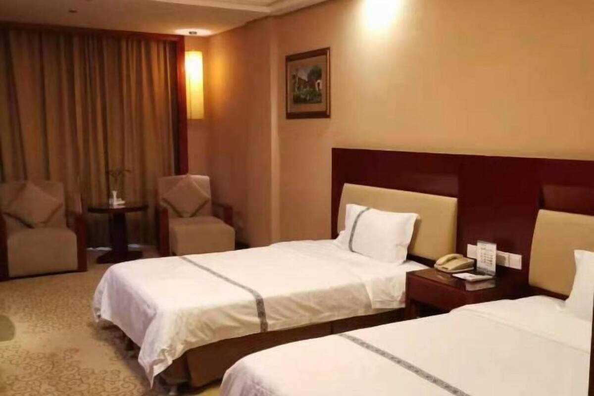 A hotel room with two beds, a nightstand with a telephone, a chair, and a small table.