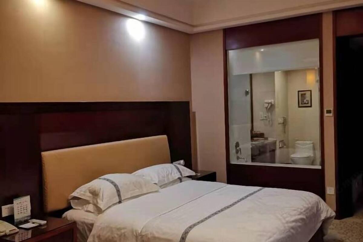 A hotel room with a bed, a nightstand, a mirror, and a door leading to a bathroom.