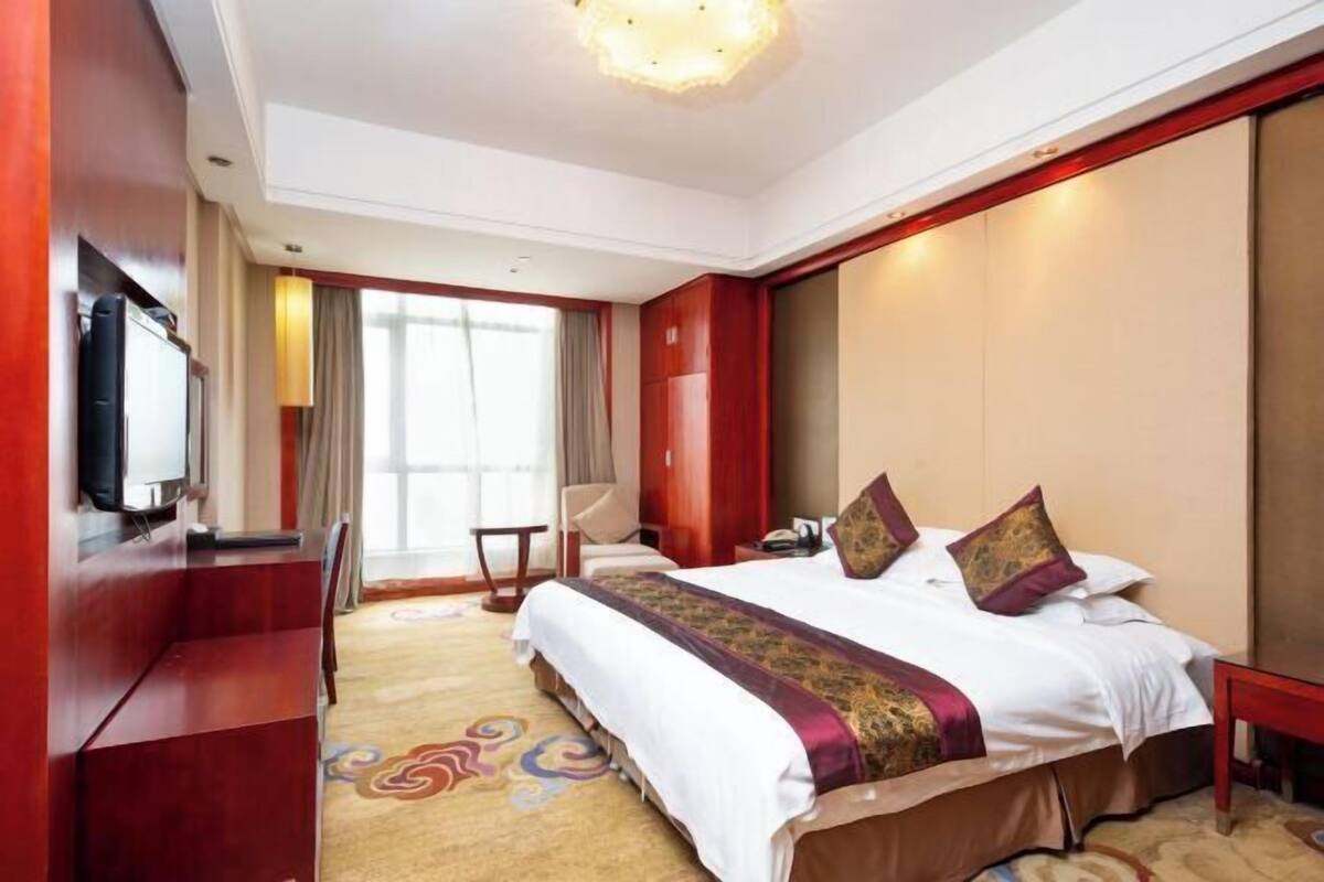 A hotel room with a large bed, a desk, a television, and a window with curtains.