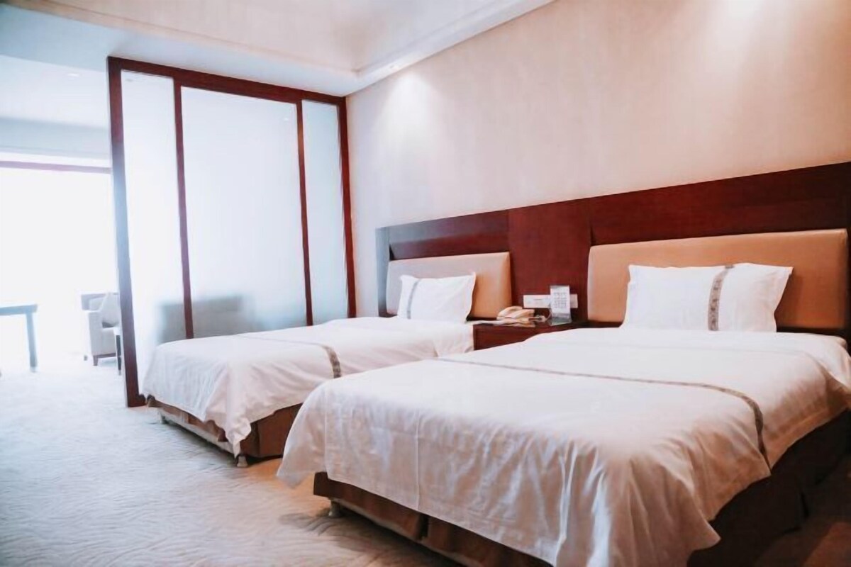 A hotel room with two beds, a wooden headboard, and a large window.
