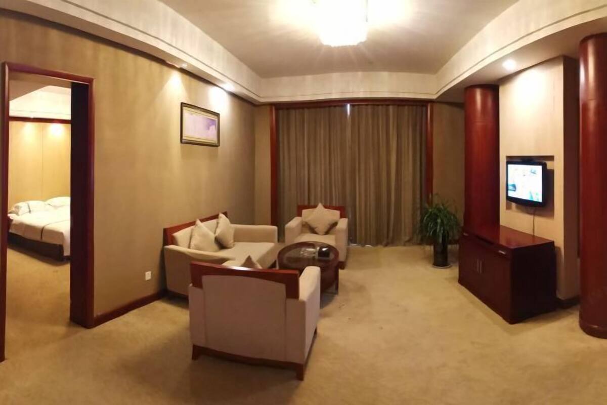 A hotel room with a living area, a bed, a TV, and a plant.