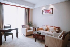 A hotel room with a dining table, two armchairs, a sofa, a coffee table, and a large window with curtains. - Runying Hotel (Tianchang)