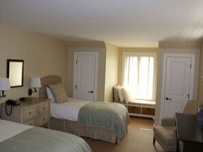 A hotel room with two beds, a desk with a lamp, a chair, and a window with curtains.