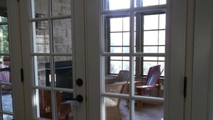 Quarto com uma grande porta de vidro que dá para uma área externa com cadeiras de vime e uma mesa de madeira.