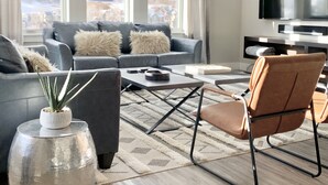 Un salon moderne avec un canapé gris, un fauteuil marron, une table basse et un téléviseur.