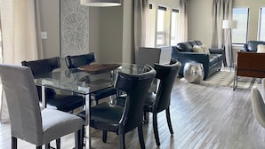 Un salon moderne avec une table à manger en verre, des chaises noires, un canapé gris et un grand lampadaire.