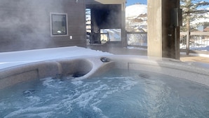Un espace avec un bain à remous offrant une vue sur un paysage enneigé, et une horloge fixée sur un poteau.