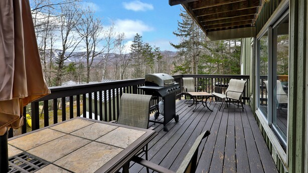 A wooden deck with outdoor seating, a grill, and a view of trees and mountains. - Heart of Killington location. Pet-friendly! (Killington)