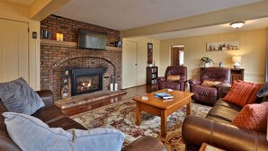A living room with a brick fireplace, leather furniture, and a flat-screen TV mounted above it. - Heart of Killington location. Pet-friendly! (Killington)