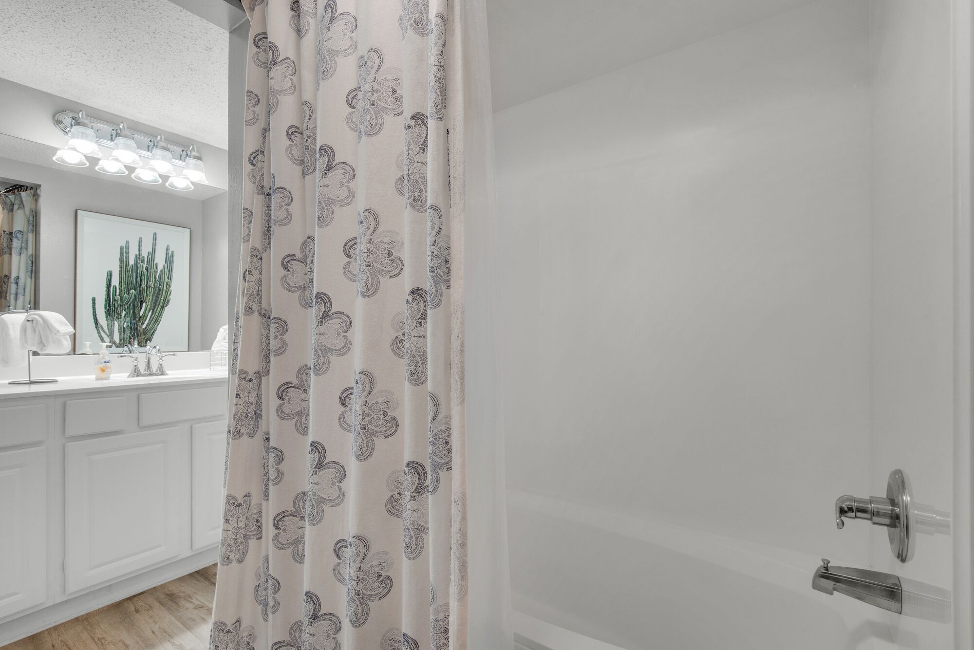 A bathroom with a shower curtain, a sink with a mirror, and a cactus artwork on the wall.