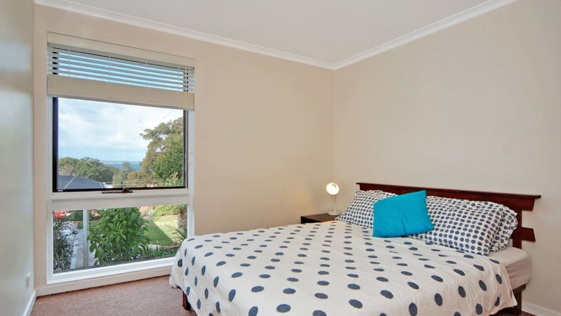 A bedroom with a bed, a nightstand, a lamp, and a window with blinds.