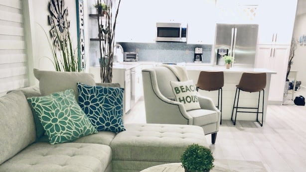 A modern living room with a sectional sofa, a round coffee table with a plant, and a kitchen in the background. - Newly Furnished! Minutes from beach, heated private pool, Elegant and Coastal!   (Naples)