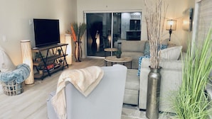 A modern living room with a flat-screen TV, sofa, coffee table, and decorative plants. - Newly Furnished! Minutes from beach, heated private pool, Elegant and Coastal!   (Naples)