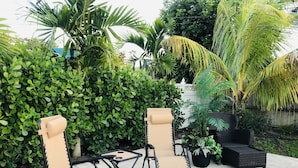 Two beige folding chairs with black frames and a small table, set on a paved patio surrounded by lush green foliage and a white fence. - Newly Furnished! Minutes from beach, heated private pool, Elegant and Coastal!   (Naples)