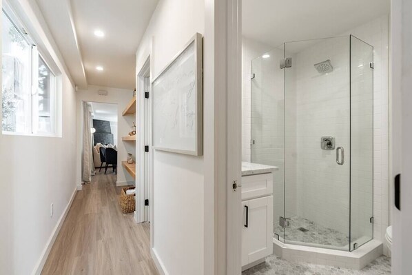 Une salle de bain moderne avec une douche à parois de verre, des murs recouverts de carreaux blancs et un plancher en bois.