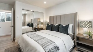 Ein modernes Schlafzimmer mit einem großen Bett, Nachttischen, einem Spiegel und Blick ins Freie.