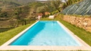 A rectangular swimming pool with a clear blue water surface, surrounded by a well-maintained grassy area and a stone wall. - Douroparadise (Caldas de Moledo)