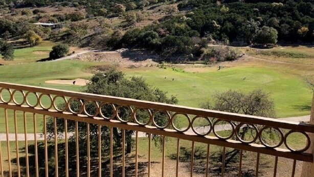 Ein Golfplatz mit Blick auf einen Hügel, der mit Bäumen und einem Gebäude in der Ferne bewachsen ist.