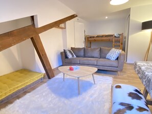 A cozy living room with a sofa, a small table, a yellow couch, and a wooden bunk bed.