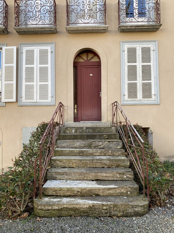 A building with a red door, white shutters, and a stone staircase with metal railings.