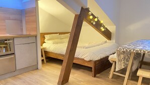 Un dormitorio pequeño con techo inclinado, una cama, una mesita y un rincón americano.