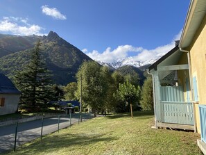 A residential area with a house featuring a porch and a mountain backdrop. - Joli chalet 60m2 proche du centre. parking. balcon (Cauterets)