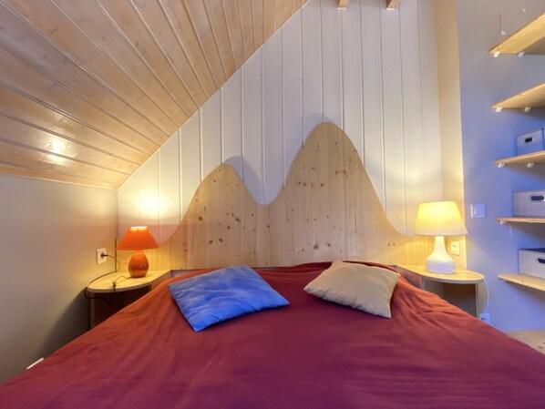 A bedroom with a wooden headboard, a red bedspread, two pillows, and bedside lamps.