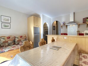 A compact living space with a sofa, a dining table, a built-in kitchen with a refrigerator, and a chimney. - Joli chalet 60m2 proche du centre. parking. balcon (Cauterets)