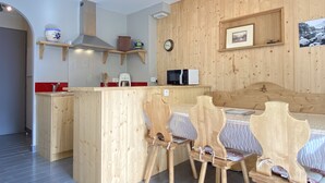 A wooden interior with a kitchen area, wooden chairs, a microwave, and a clock on the wall.