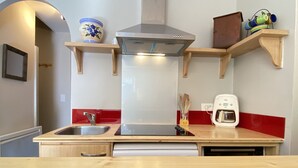 A kitchen with a stainless steel range hood, wooden shelves, a coffee maker, and a sink.