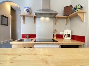 A kitchen with a stainless steel range hood, wooden shelves, a coffee maker, and a sink.