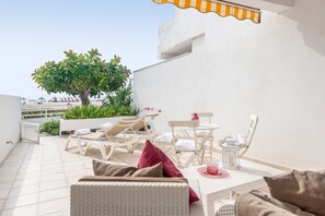 Een terras op het dak met een witte wickerbank, een eettafel met stoelen en een kleine boom.