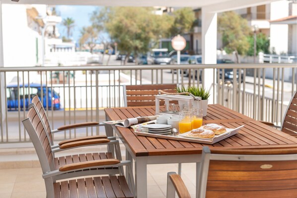 A wooden table with breakfast items, including croissants and orange juice, on a balcony with a view of the street and buildings.
