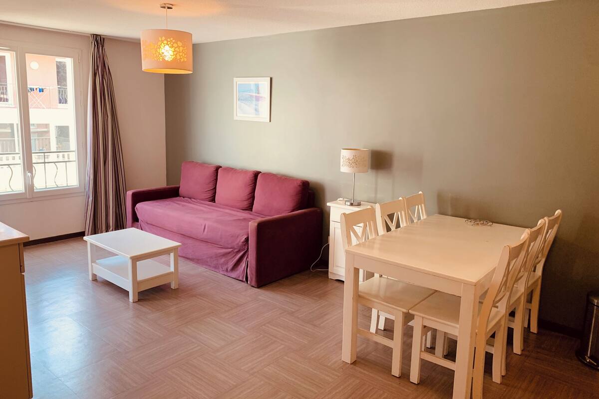 Un salon comprenant un canapé, une petite table, une table à manger avec des chaises, une lampe et un tableau au mur.