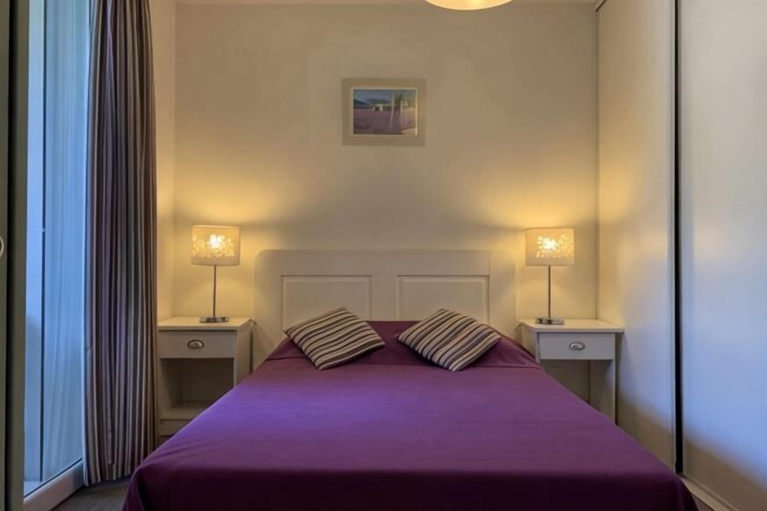 Une chambre d’hôtel avec un lit, deux lampes de chevet, une table de chevet, une tête de lit et un tableau au mur.