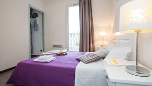 Une chambre d’hôtel comprenant un lit, une table de chevet, une lampe, une fenêtre avec des rideaux et une porte avec un porte-serviettes.