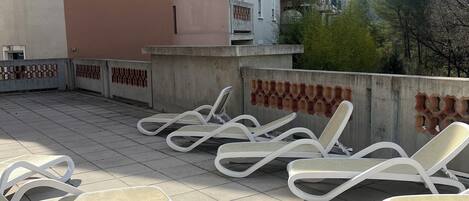 A rooftop terrace with white lounge chairs and a view of a pink building with balconies.