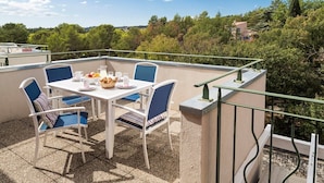 Un balcon avec une table dressée pour le petit-déjeuner, entouré de chaises, offrant une vue sur un paysage luxuriant.
