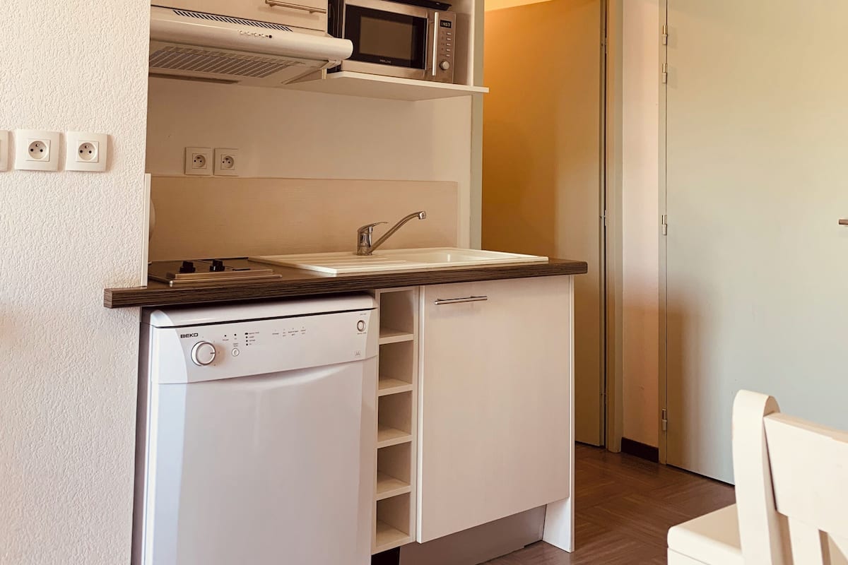 Une cuisine compacte équipée d’un four à micro-ondes encastré, d’un lave-vaisselle et d’un petit plan de travail.