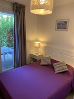 Un dormitorio con una colcha morada, almohadas a rayas, una lámpara de noche y un cuadro en la pared.