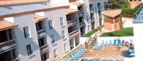Un hotel de varios pisos con piscina en la azotea, mobiliario exterior y vistas del paisaje circundante.