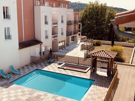 Un área de piscina con suelo de baldosas, sillas de descanso y un pérgola de madera.
