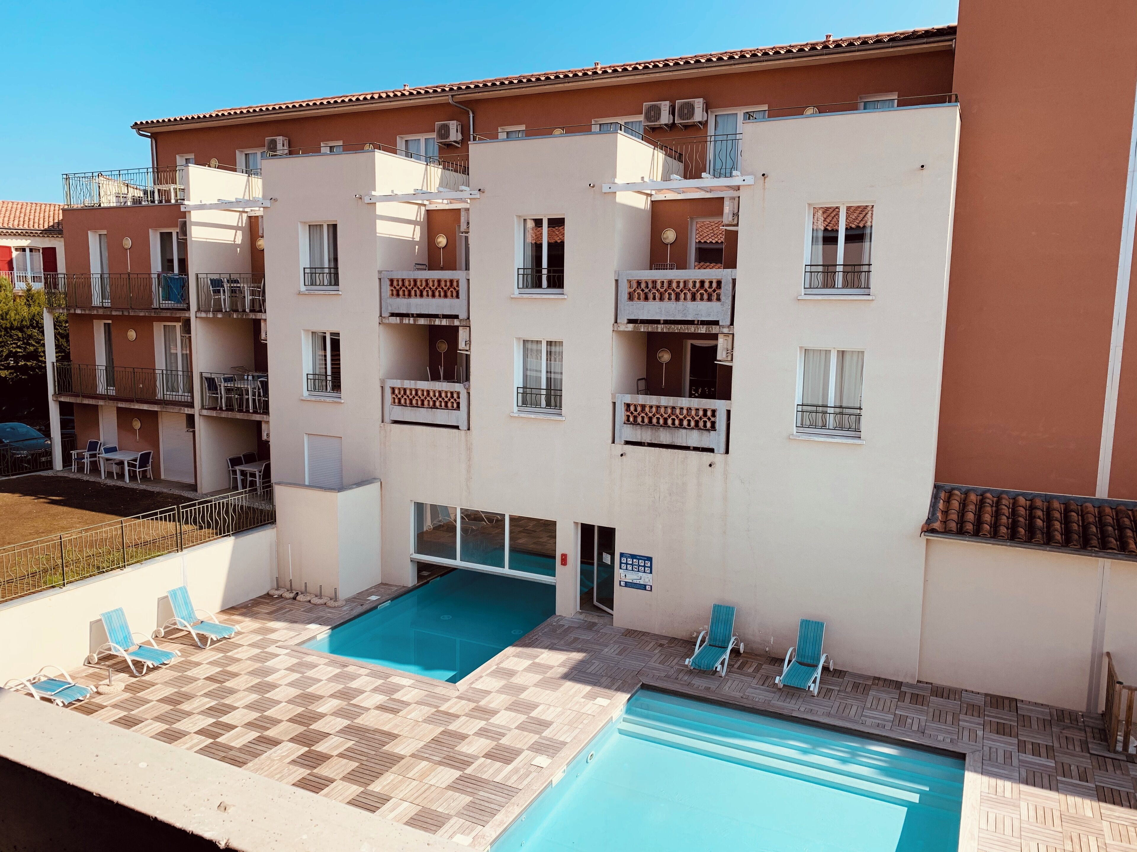 A multi-story residential building with balconies, a swimming pool, and outdoor seating.