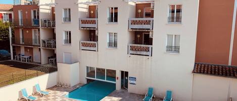 A multi-story residential building with balconies, a swimming pool, and outdoor seating.