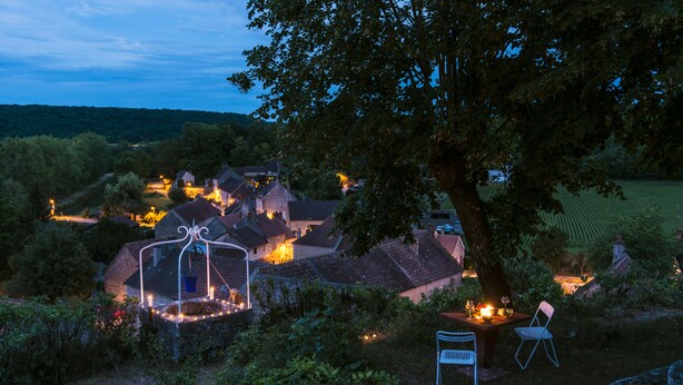 A rural village at dusk with houses, a tree, and a table with chairs under the tree. - Le Domaine des Carriers - Gîtes (Chevroches)