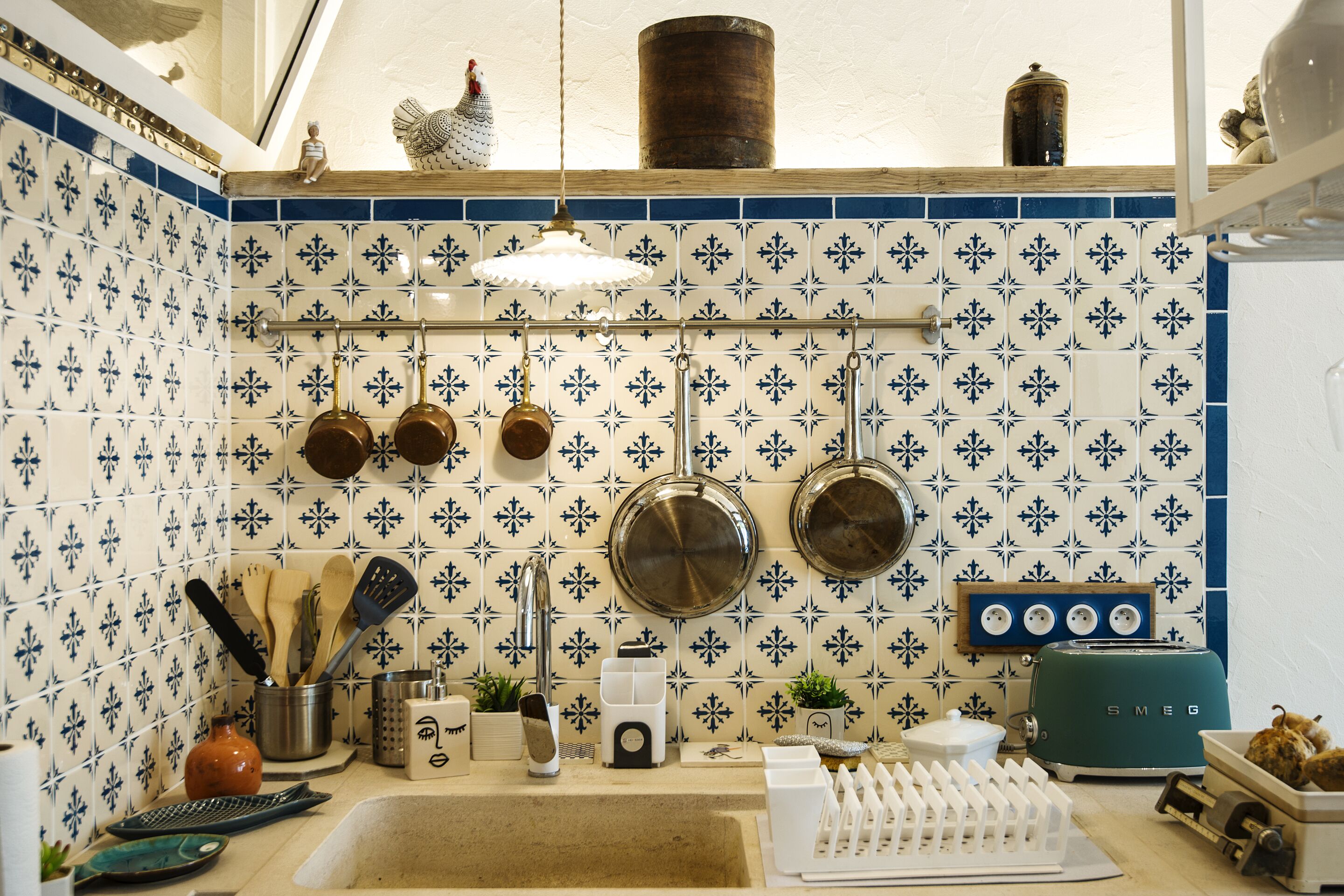 Una cocina con baldosas azules y blancas estampadas, ollas colgantes, un lavamanos y un tostador de estilo vintage.