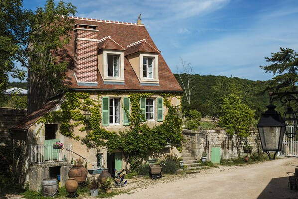 A traditional house with a sloped roof, green shutters, and a stone wall.
