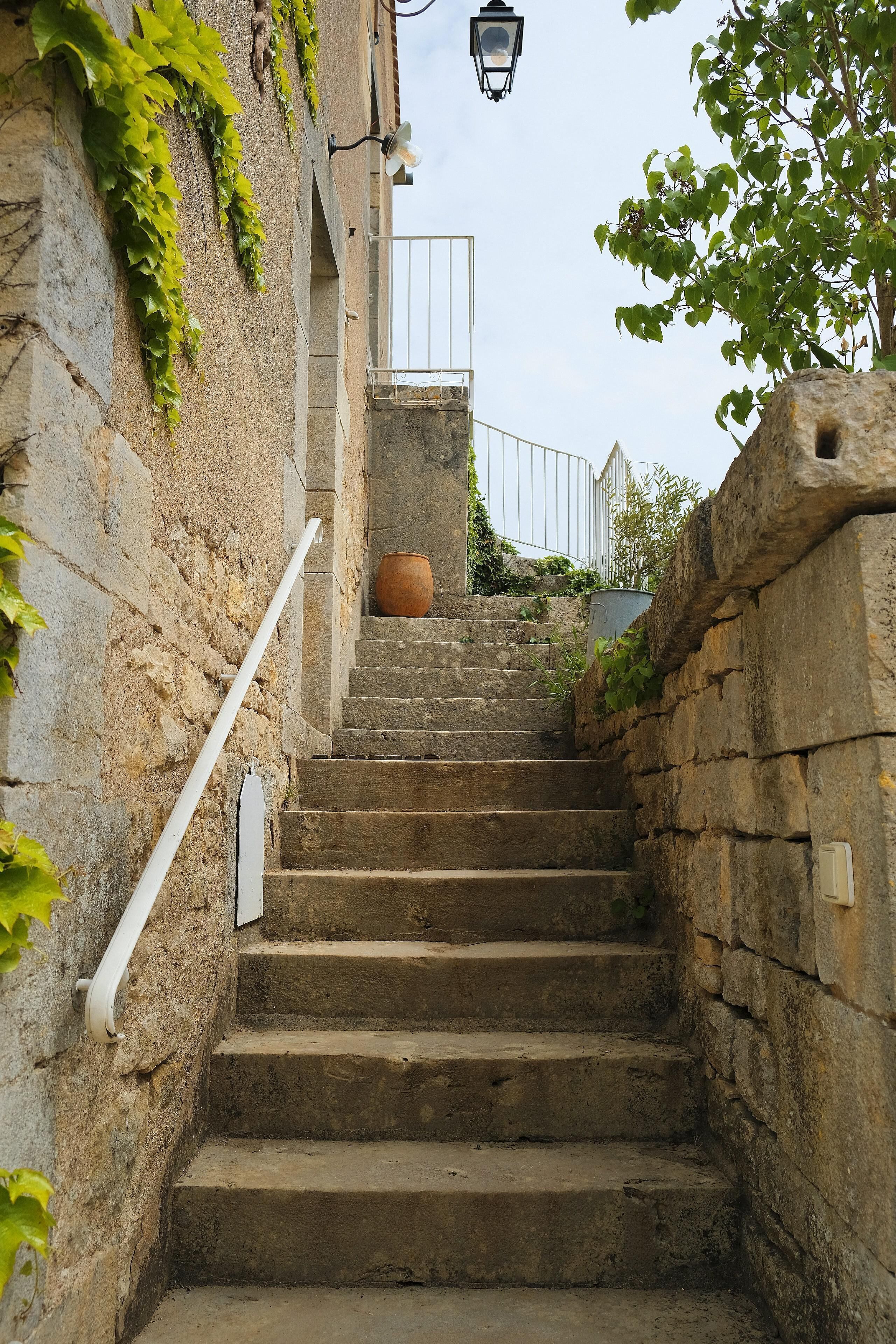 Un escalier en pierre avec une main courante blanche, menant à une balustrade blanche et à une lanterne.