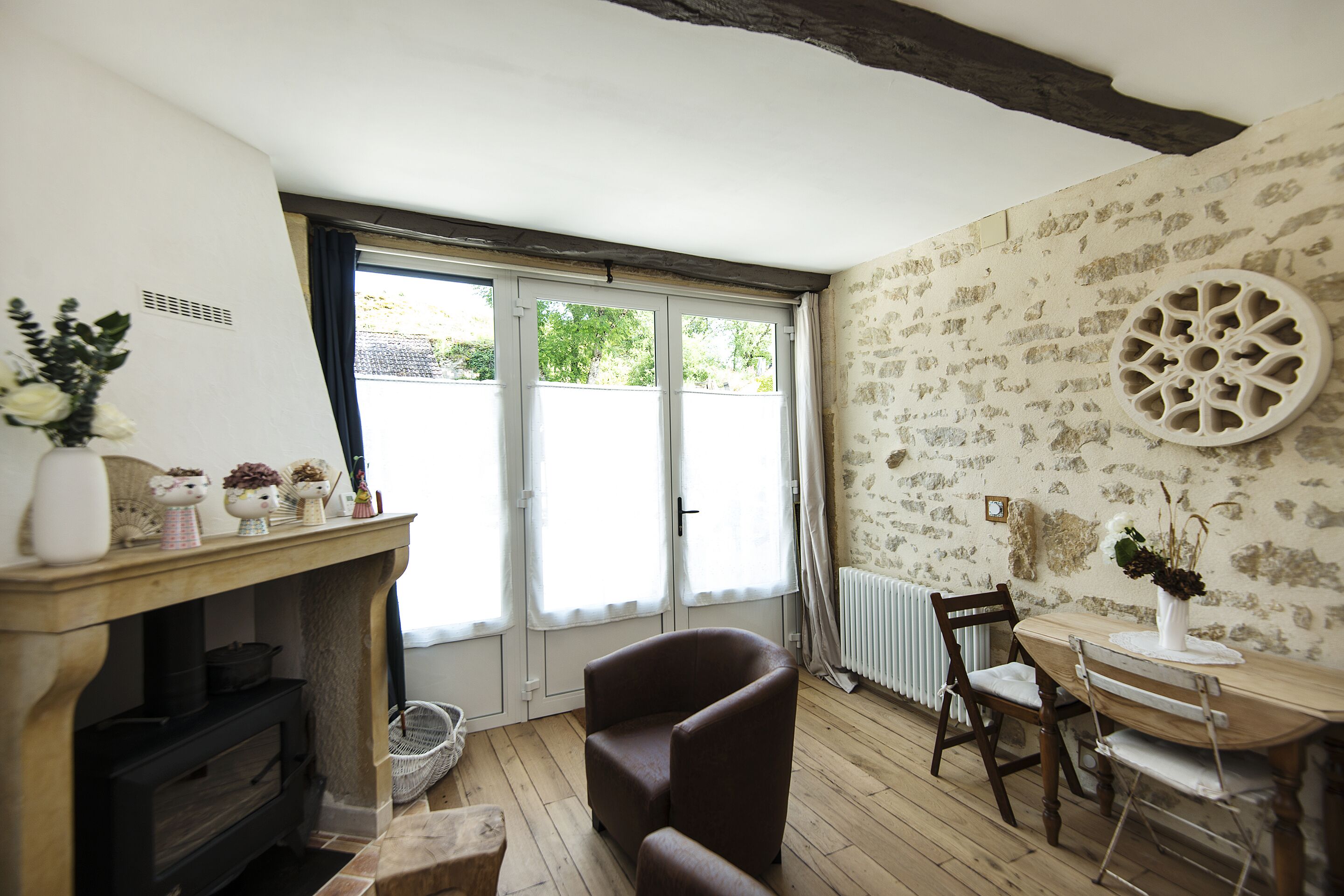 A room with a fireplace, a dining table with chairs, a window with curtains, and a patterned wall.